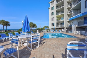 A poolside area with lounge chairs and umbrellas, a pool, and a building with balconies.