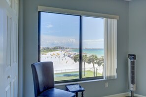 A room with a large window overlooking a beach, a chair, and a standing heater.