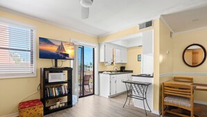 A modern kitchen with white cabinets, a microwave, and a dining area with a table and chairs. - Gulf Winds 508 | Affordable Studio on Upham Beach (ST PETE BEACH)