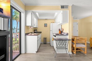 A modern kitchen with white cabinets, a small island, a trash bin, and a dining area with a table and chairs.