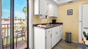 A kitchen with white cabinets, a black countertop, and a stainless steel sink. - Gulf Winds 508 | Affordable Studio on Upham Beach (ST PETE BEACH)