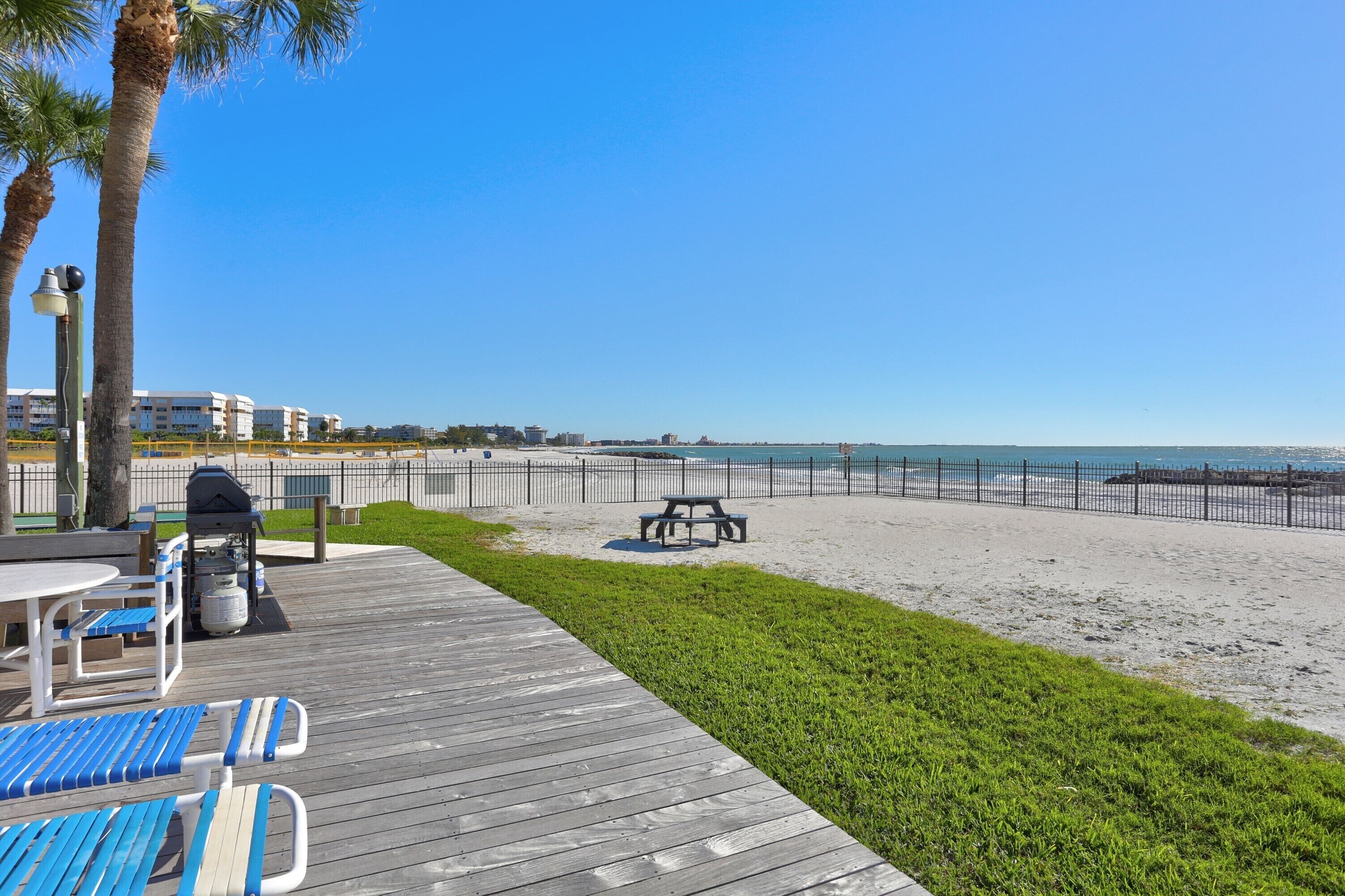 A beachside patio with a wooden deck, picnic table, and lounge chairs.