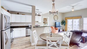 A modern kitchen with white cabinets, a dining area with a round table and chairs, and a living area with a sofa and TV.