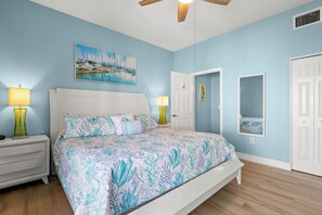 Une chambre à coucher avec un lit, des tables de chevet, un ventilateur de plafond et un tableau accroché au mur.