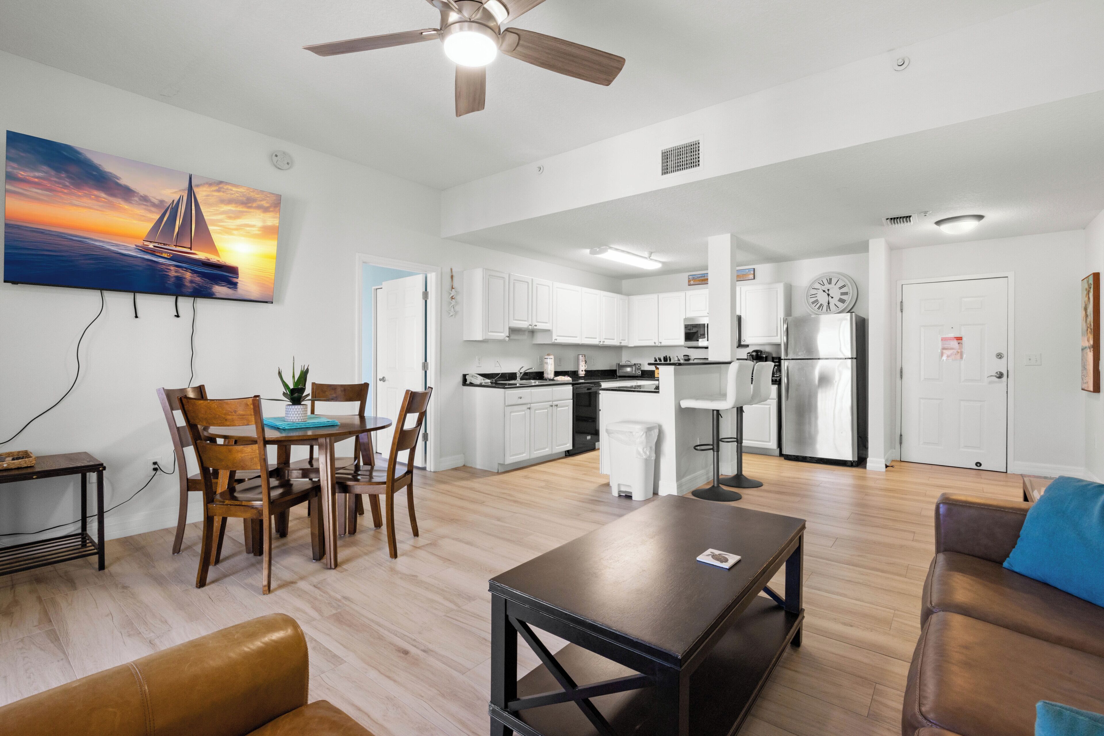 A modern living room with a dining area, kitchen, and a ceiling fan.