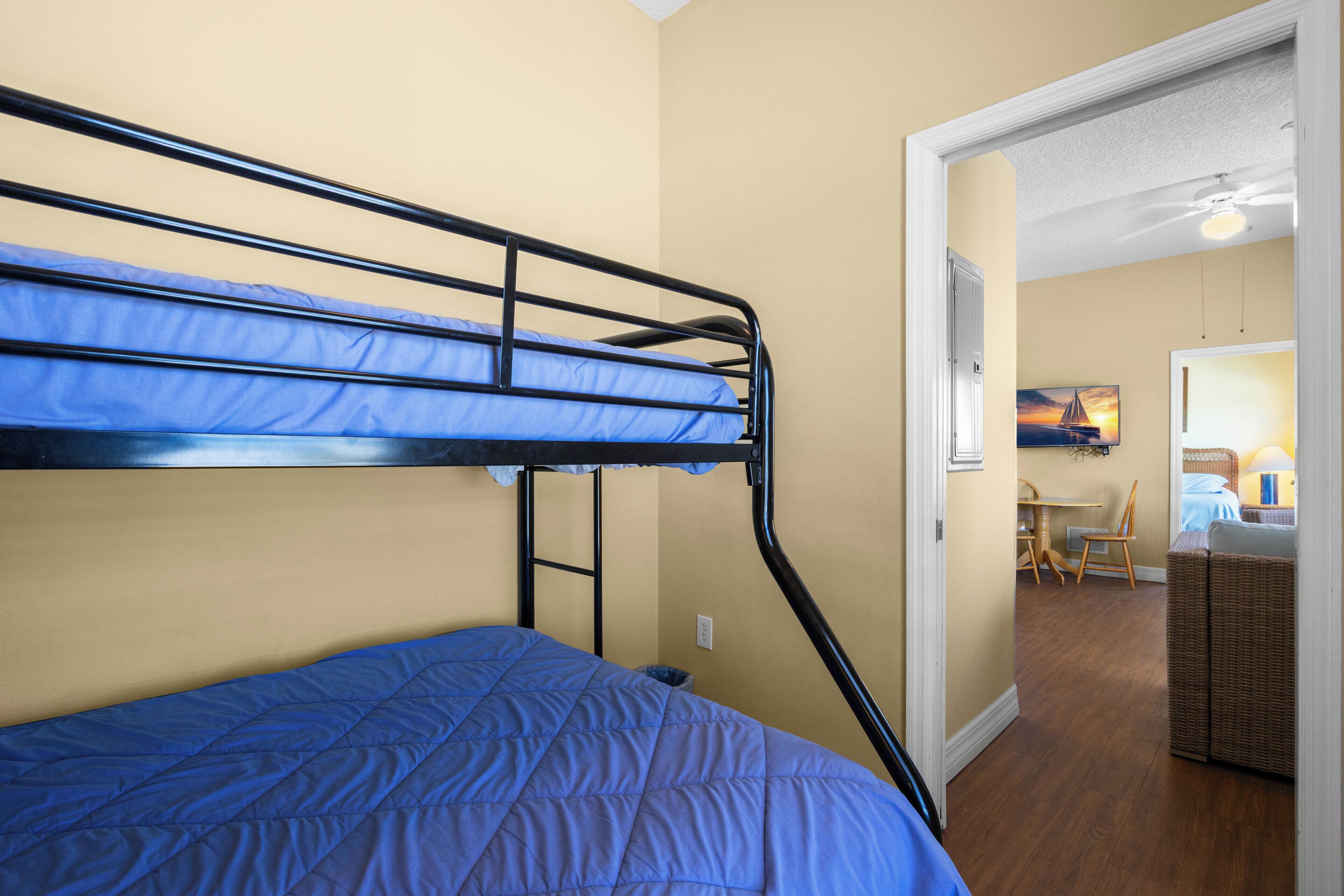 A bunk bed with blue bedding, a dining area with a table and chairs, and a wicker chair.