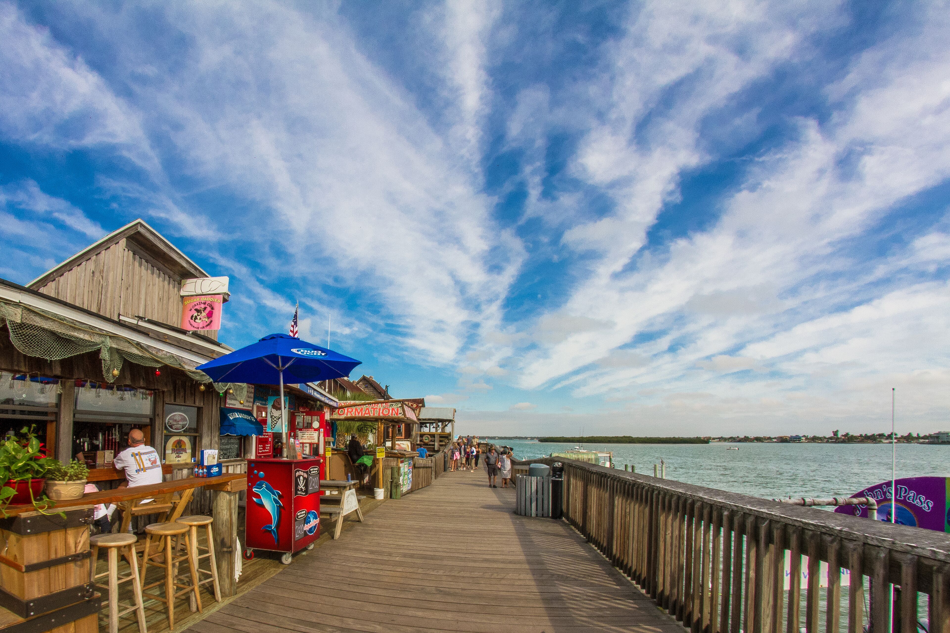 A wooden pier with a view of the water, a bar area with stools, and a sign for 'John's Pass'.