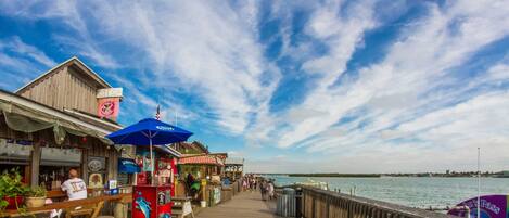 A wooden pier with a view of the water, a bar area with stools, and a sign for 'John's Pass'.