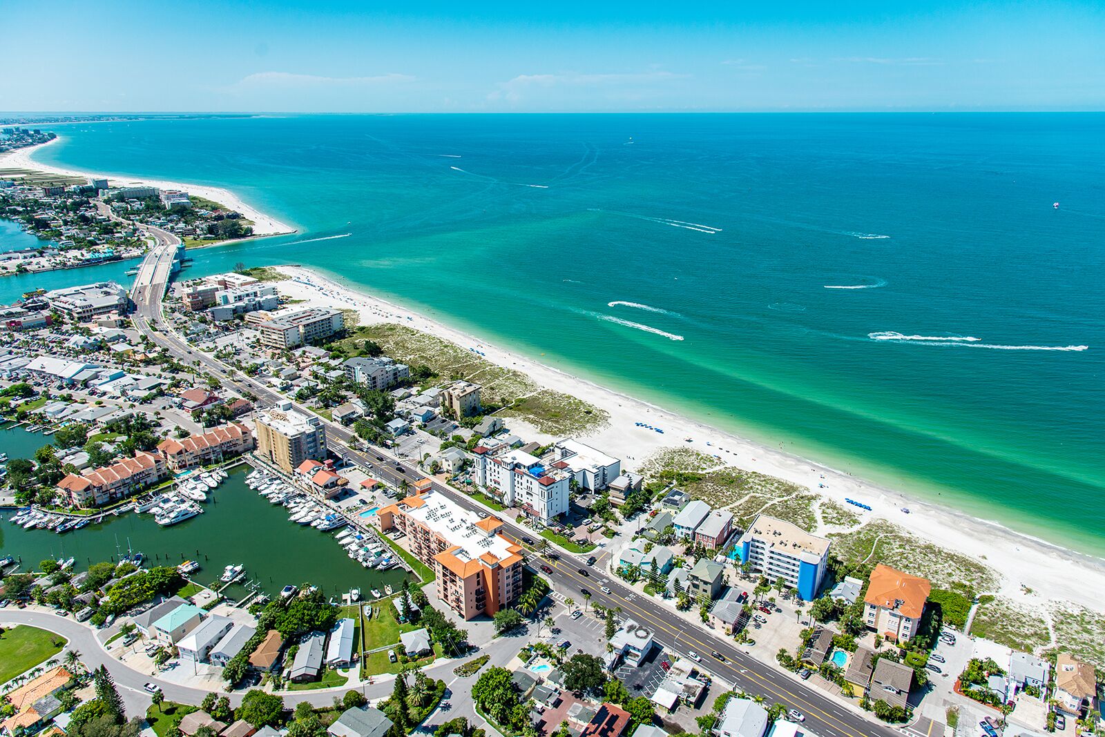 An aerial view of a coastal city with a marina, buildings, and a beach.