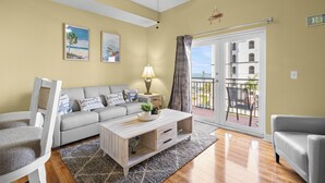 A living room with a sofa, a coffee table, a lamp, and a view of the outside. - ♿ Madeira Bay Resort #402 – Spacious, Handicap-Friendly One-Bedroom Retreat Near the Beach (Madeira Beach)