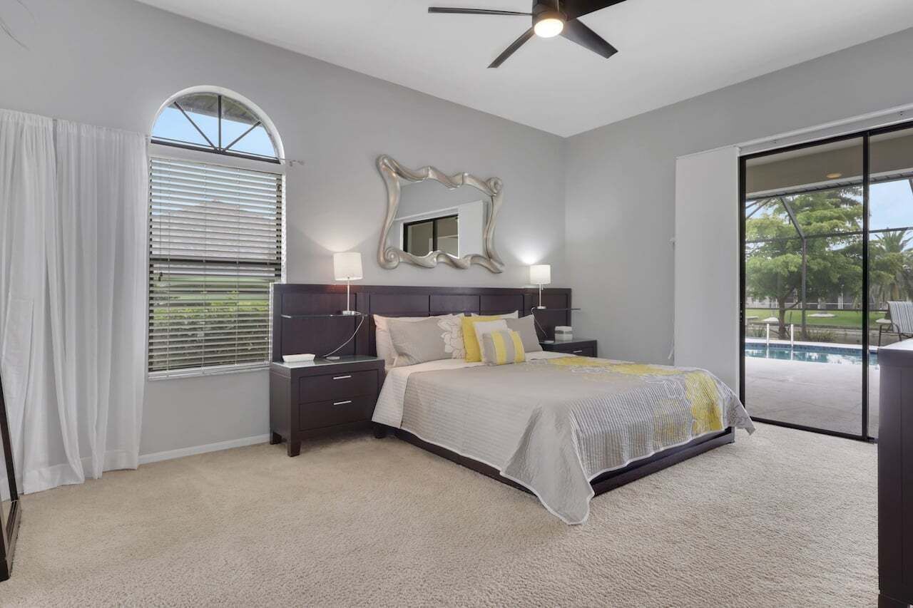Une chambre à coucher avec un lit, une table de chevet, un miroir et un ventilateur de plafond.