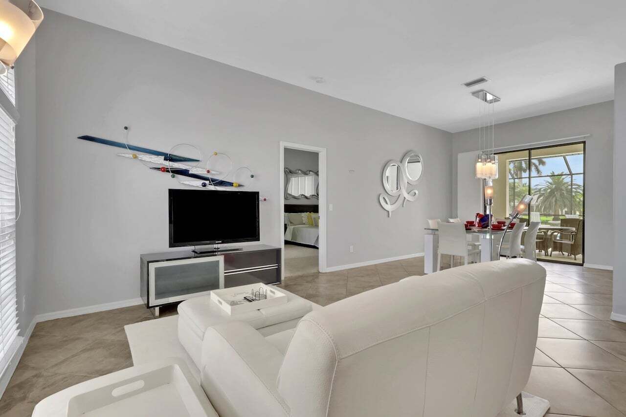 A modern living room with a flat-screen TV, a sofa, and a dining area with a table and chairs.