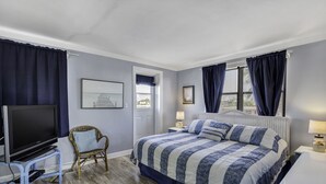 A bedroom with a bed, a television, a chair, and a window with curtains. - 🌅 Gulf Winds 2BR Condo — Rooftop Deck with Stunning Beach Views (St Pete Beach)