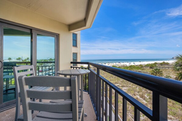 A balcony with a view of the beach, a table, and two chairs.