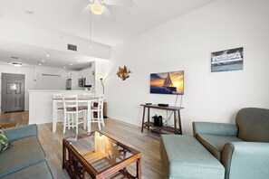 A modern living room with a glass coffee table, a sofa, a dining area with chairs, and a kitchen in the background. - 🌴 Madeira Bay Resort #206 – Family-Friendly Comfort with Balcony & Beach Access (Madeira Beach)