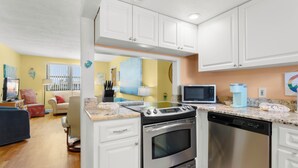 A modern kitchen with white cabinets, stainless steel appliances, and a marble countertop. - Gulf Winds 1505 — Updated Tile Floors & Room for Everyone (St Pete Beach)