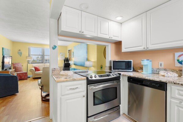 A modern kitchen with white cabinets, stainless steel appliances, and a marble countertop. - Gulf Winds 1505 — Updated Tile Floors & Room for Everyone (St Pete Beach)