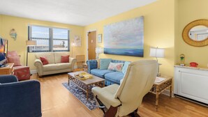 A living room with a sofa, armchairs, a coffee table, and a painting on the wall. - Gulf Winds 1505 — Updated Tile Floors & Room for Everyone (St Pete Beach)
