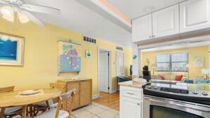 A kitchen with a dining area, white cabinets, a stove, and a ceiling fan. - Gulf Winds 1505 — Updated Tile Floors & Room for Everyone (St Pete Beach)