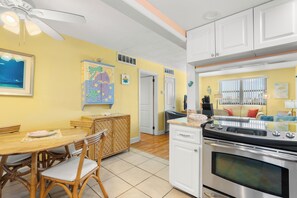 A kitchen with a dining area, white cabinets, a stove, and a ceiling fan.