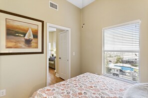 A bedroom with a bed, a painting of a sailboat, a door leading to another room, and a window with blinds.