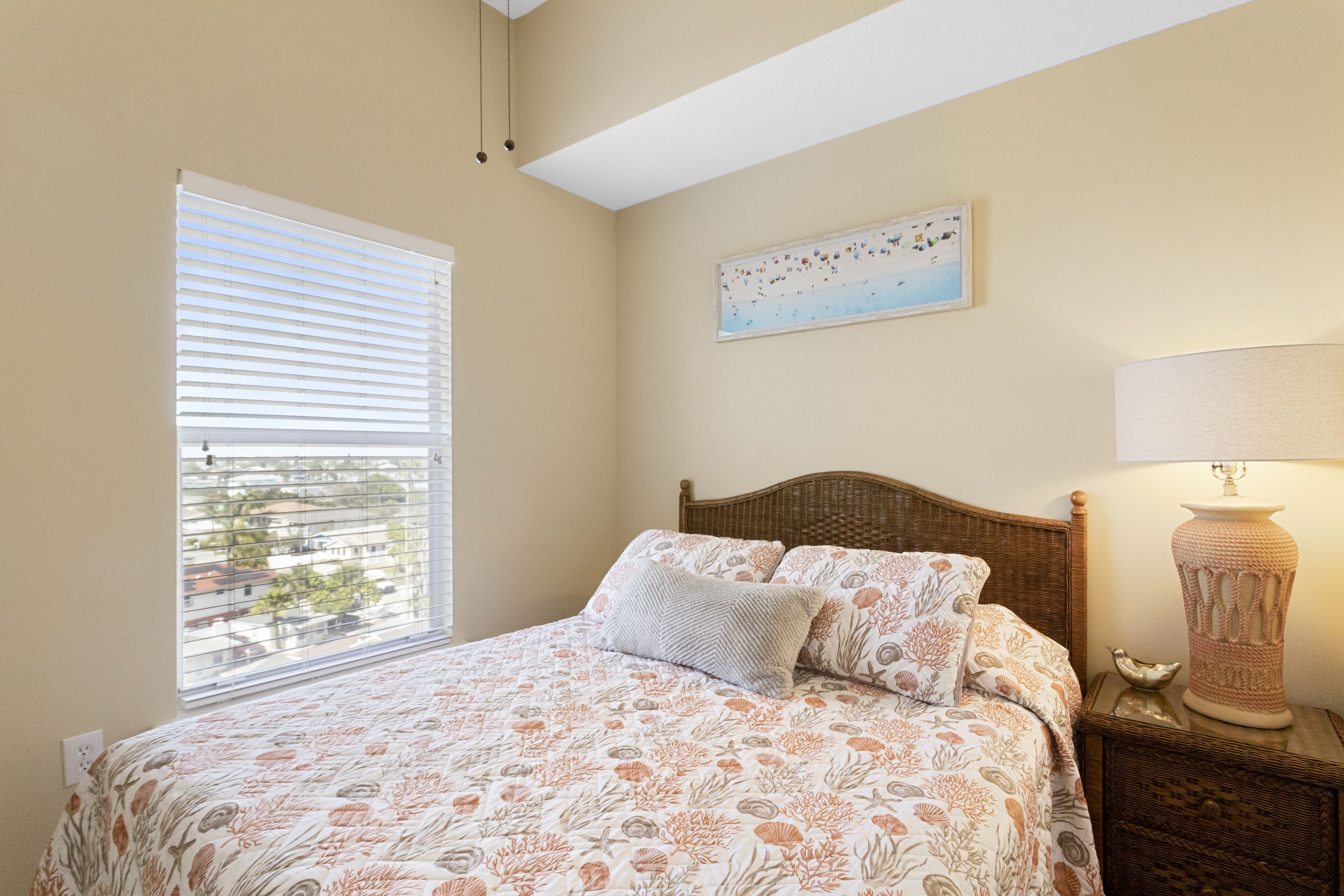 A bedroom with a bed, a window with blinds, a wall-mounted lamp, and a painting.