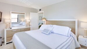 A modern hotel room with a large bed, a bedside table, a mirror, and a nightstand. - 🌅 Gulf Winds 2nd-Floor Condo — Gulf Views & Bright Beachside Charm (ST PETE BEACH)