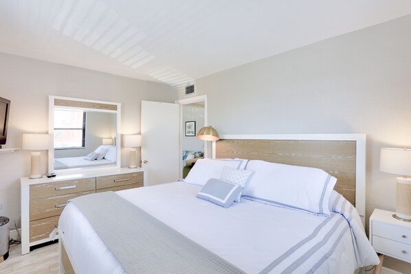 A modern hotel room with a large bed, a bedside table, a mirror, and a nightstand.