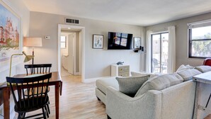 A modern living room with a sofa, a dining table with chairs, a TV, and artwork on the walls. - 🌅 Gulf Winds 2nd-Floor Condo — Gulf Views & Bright Beachside Charm (ST PETE BEACH)