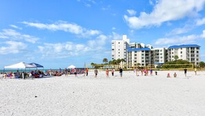 A beach with a volleyball net, a white tent, and a hotel in the background. - 🌊 Caprice Resort Unit #203 – Gulf Front Serenity for Two in St. Pete Beach (St Pete Beach)