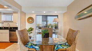 A dining area with wicker chairs, a glass table, and a decorative plant centerpiece. - 🌊 Caprice Resort Unit #203 – Gulf Front Serenity for Two in St. Pete Beach (St Pete Beach)