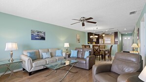 A living room with a sofa, armchair, glass coffee table, and a ceiling fan.