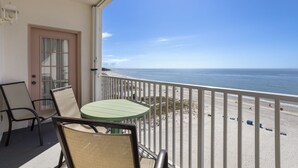 A balcony with a view of the beach, a door, and two chairs.