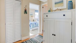 A hallway with a closed white closet, a bed with a blue and white bedspread, and a painting on the wall. - 🌊 Gulf Winds 2BR Condo — Partial Gulf Views, Remodeled Bath & Steps to the Sand (ST PETE BEACH)