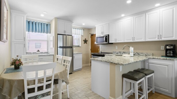 A modern kitchen with white cabinetry, a stainless steel refrigerator, a microwave, and a granite countertop. - 🌊 Gulf Winds 2BR Condo — Partial Gulf Views, Remodeled Bath & Steps to the Sand (ST PETE BEACH)