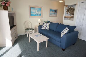 A living room with a blue sofa, a small white table, a white chair, and a TV on a stand.