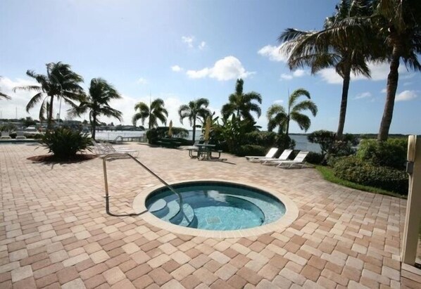 Ein Pool mit Backstein-Terrasse, umgeben von Palmen und Blick aufs Meer.