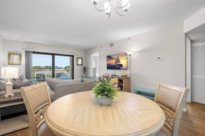 A modern living room with a round dining table, a sofa, a TV, and a balcony with a view.