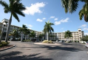 Un hotel de varios pisos con un patio central, palmeras y un cielo azul despejado.