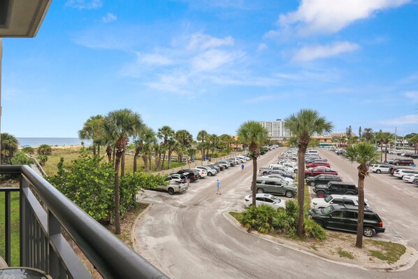 A parking lot with multiple cars, palm trees, and a view of the beach.