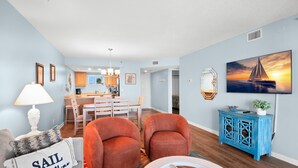 Ein Wohnzimmer mit einer Couch, zwei Sesseln, einem Couchtisch und einem blauen Schrank. Im Hintergrund ist eine Essecke mit Tisch und Stühlen zu sehen.