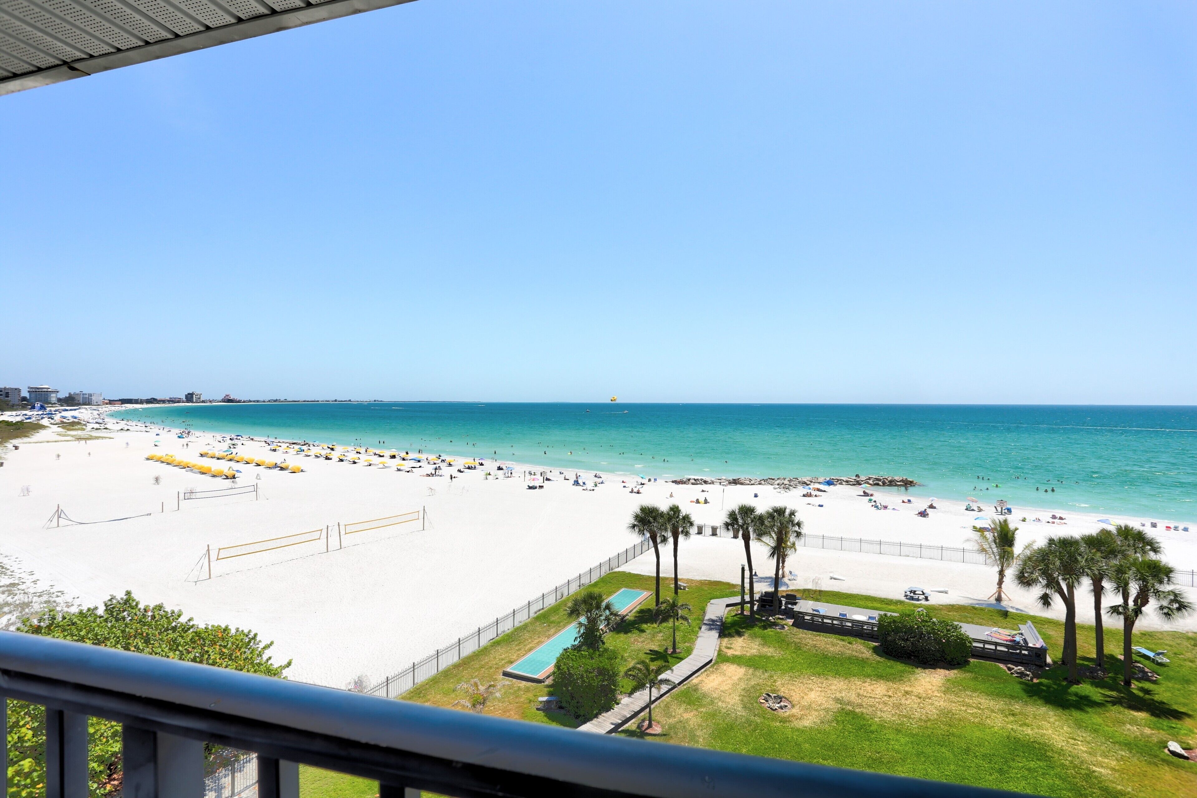 Una spiaggia con piscina, palme e un cielo azzurro intenso.