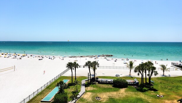A beach with a pool, palm trees, and a clear sky. - 🌞 Caprice Resort Unit #502 – Renovated Gulf Front Escape for Four Guests (St Pete Beach)