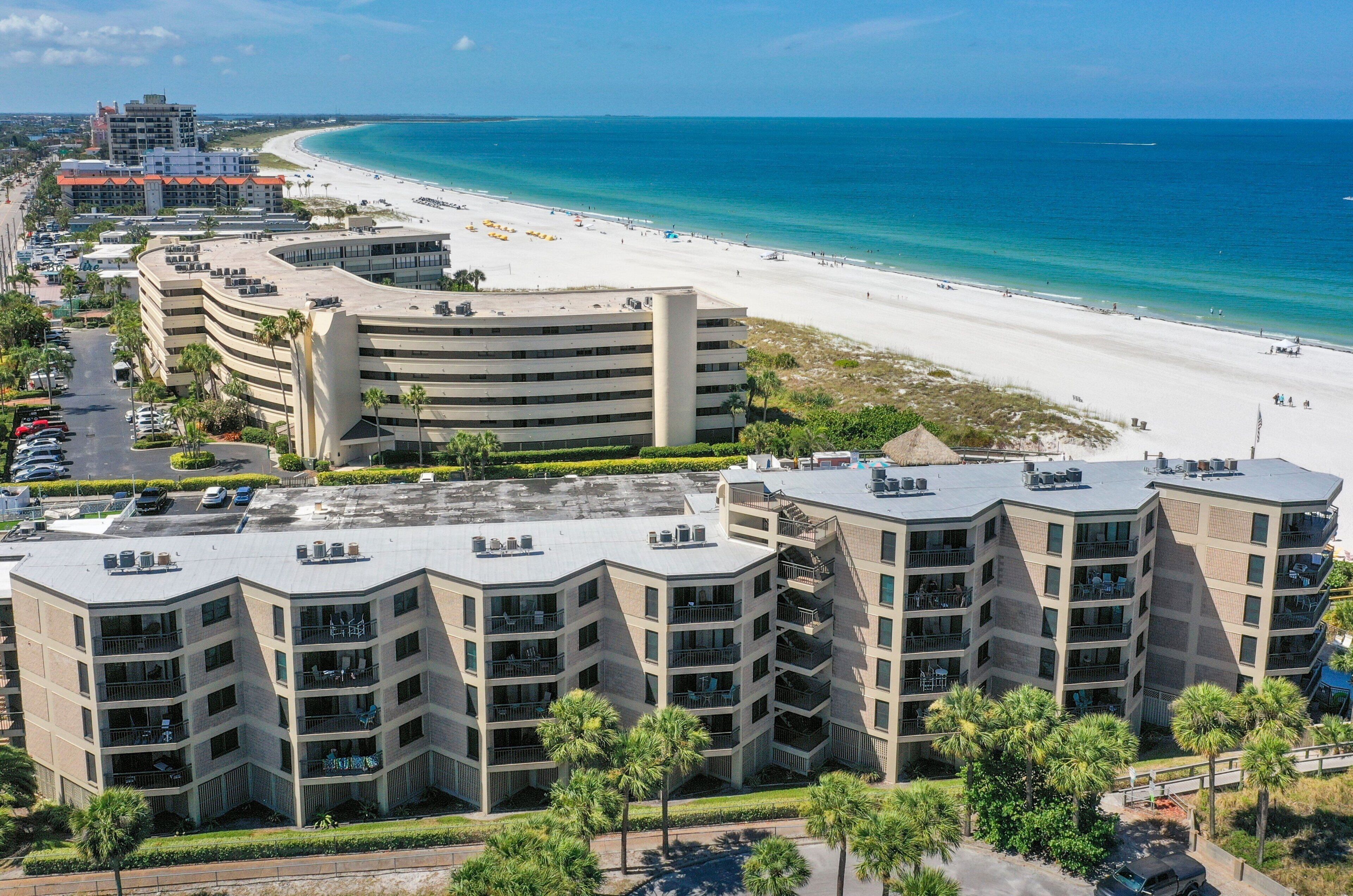 A beachfront hotel with multiple balconies, a parking lot, and a view of the beach and ocean.