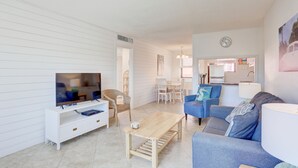 Un salon moderne doté d’un téléviseur à écran plat, d’une table basse en bois, d’un canapé bleu et d’un coin repas avec des chaises et une table.