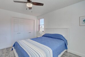 Un dormitorio con cama, paredes blancas, ventilador de techo, ventana y puerta.