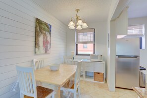 Una cocina con gabinetes blancos, un refrigerador de acero inoxidable, una mesa de comedor con sillas y un colgante de luz.