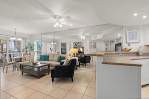 A spacious living area with a large sofa, coffee table, and dining table. There is a kitchen area with a counter and a refrigerator.