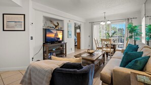 A living room with a television, sofa, coffee table, and dining area. - 🌿 Select View Condo at Gulf Strand Resort — St. Pete Beach (St Pete Beach)