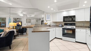 A modern kitchen with white cabinets, a microwave, stove, and a dining area with a table and chairs. - 🌿 Select View Condo at Gulf Strand Resort — St. Pete Beach (St Pete Beach)